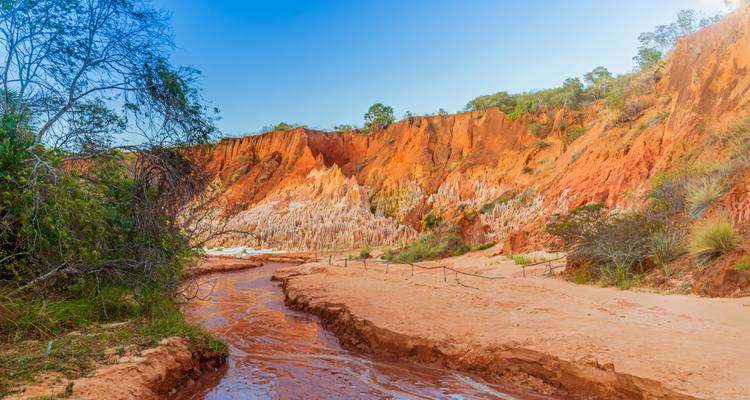 Cañón colorido y erosionado con agujas de piedra caliza roja y blanca al lado de un arroyo poco profundo.