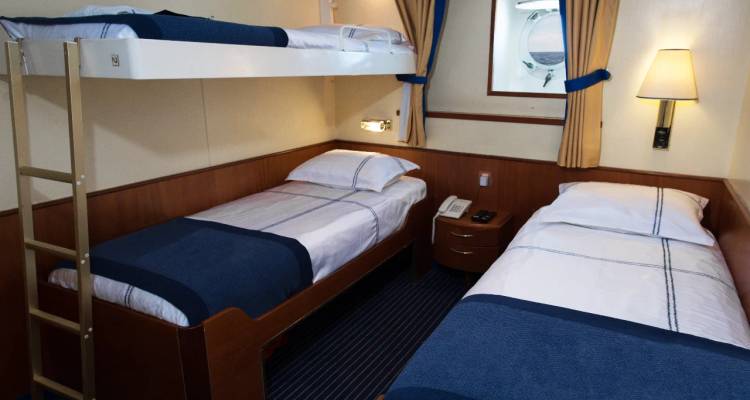 Kabine auf einem Kreuzfahrtschiff mit einem Etagenbett über zwei unteren Einzelbetten und einer kleinen Leiter.