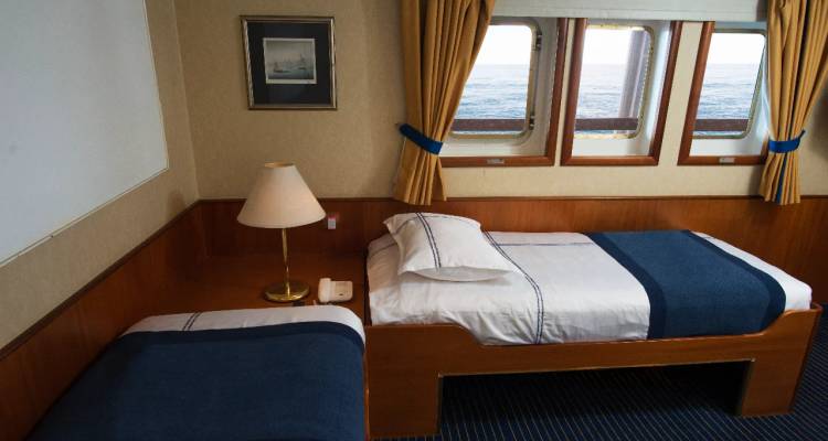 Einzelbett-Kreuzfahrtkabine mit Fensterblick auf das offene Meer und einfacher Einrichtung.