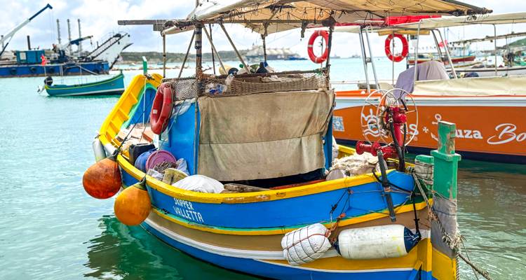 Kleurrijke Maltese visserboot afgemeerd in een rustige turkooizen haven met uitrusting en boeien aan boord.