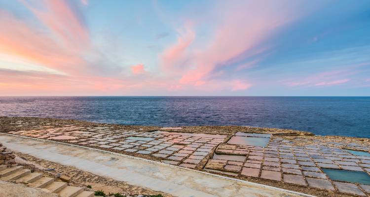 Roze en blauwe zonsondergang boven vierkante stenen zoutpannen en de open zee.