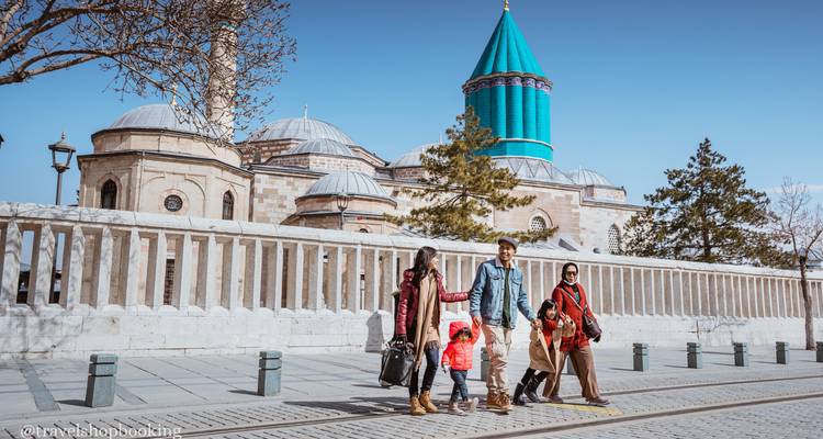 Family posing in front of the turquoise-tiled Mevlana Museum in Konya; visible watermark bottom left.