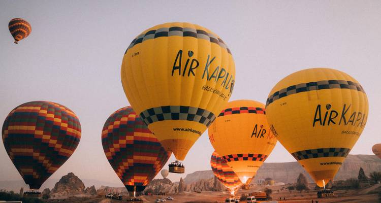 Brightly coloured hot-air balloons rise over Cappadocia’s rocky landscape under soft dawn light.