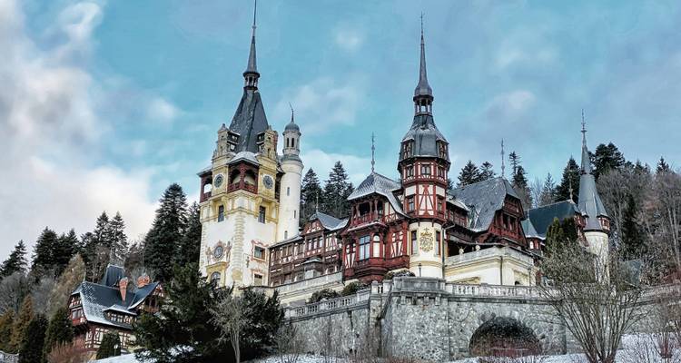 Peles Castle surrounded by lush trees and a clear sky.