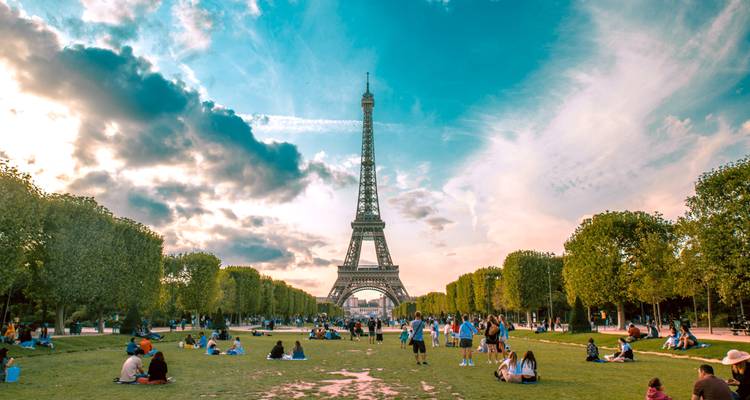 Des foules se détendant sur le Champ de Mars avec la Tour Eiffel s'élevant contre un ciel du soir dramatique.