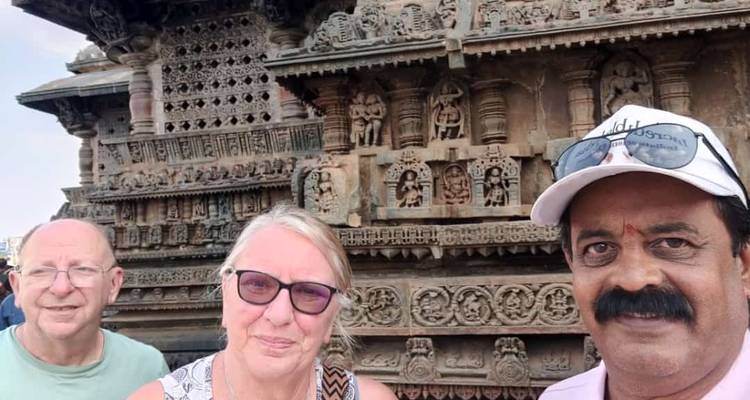 Three people posing in front of intricately carved temple wall.