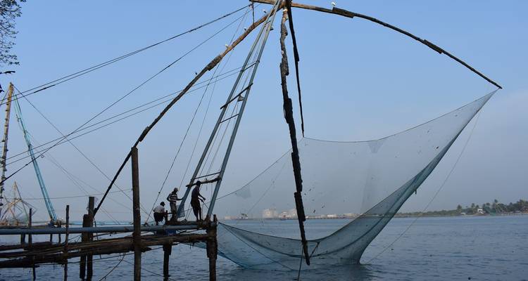 Workers maneuvering a large Chinese fishing net over water.
