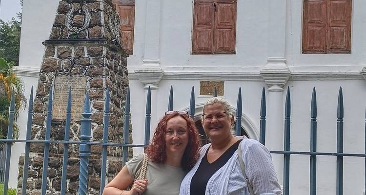 Two women in front of a colonial-style building with closed wooden shutters.
