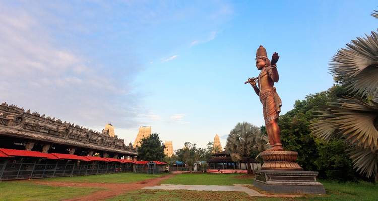 Large statue of a deity in a temple complex with an expansive garden.