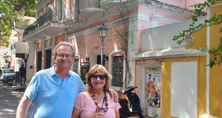 Two people posing on a tree-lined street with colorful colonial buildings.