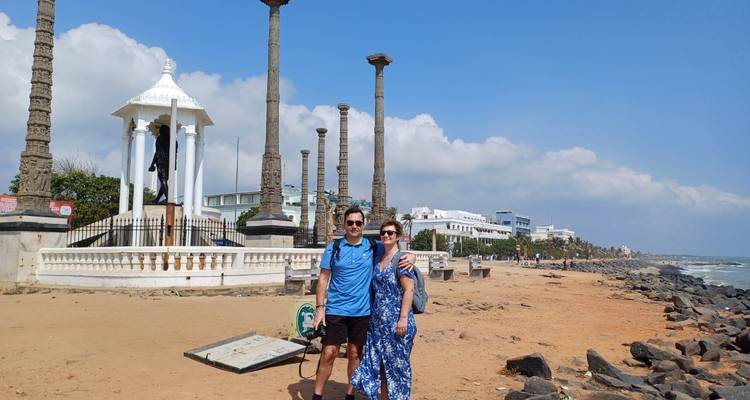Couple posing at a beach with a monument featuring multiple tall columns.