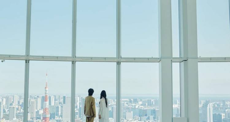 Two people standing in a tall glass building overlooking a city.