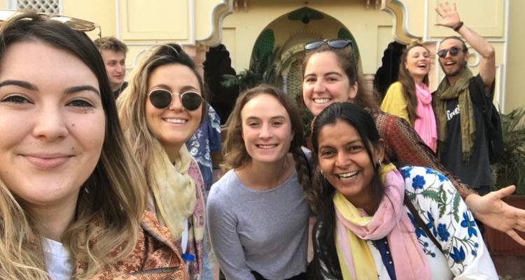 Group selfie of friends smiling with a backdrop of traditional architecture.