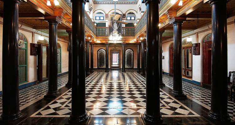 Grand interior hall with checkered floor and wooden columns.