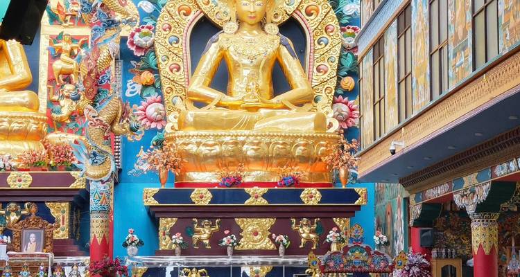 Golden seated Buddha statues amid colourful murals inside monastery hall
