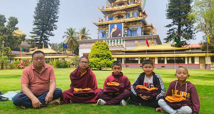 Monk children and elder seated on lawn in front of ornate Tibetan monastery