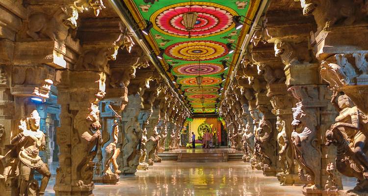 A vibrant temple corridor with intricate carvings and a colorful ceiling.