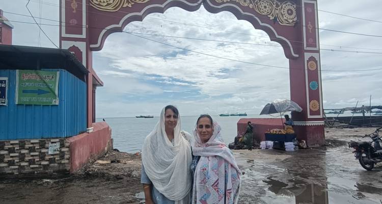Two women standing under a decorative archway by the sea.