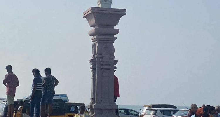 A group of people standing around a tall pillar with the sea in the background.