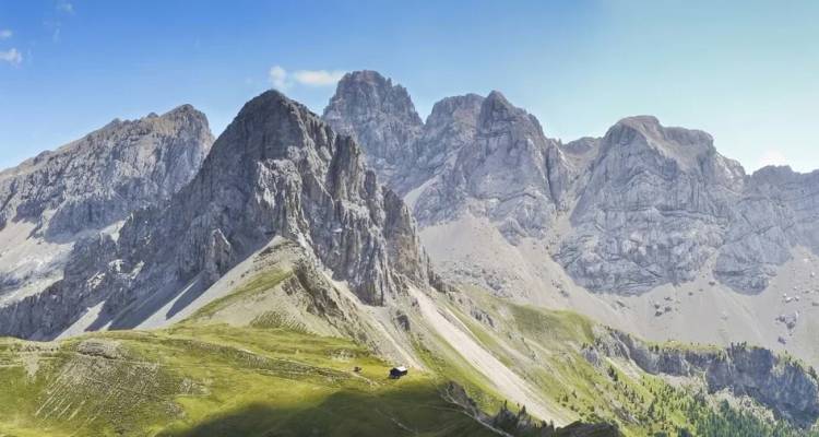 Ruige grijze pieken van de Dolomieten steken uit boven glooiende alpenweiden met hier en daar een eenzaam hutje.