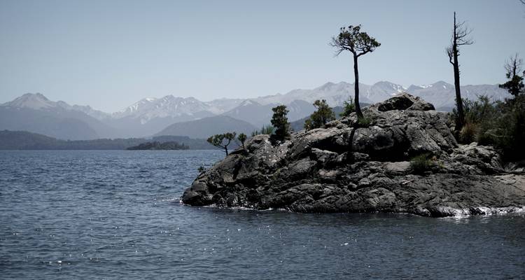 Lake with rock formations and distant mountains under a clear sky.