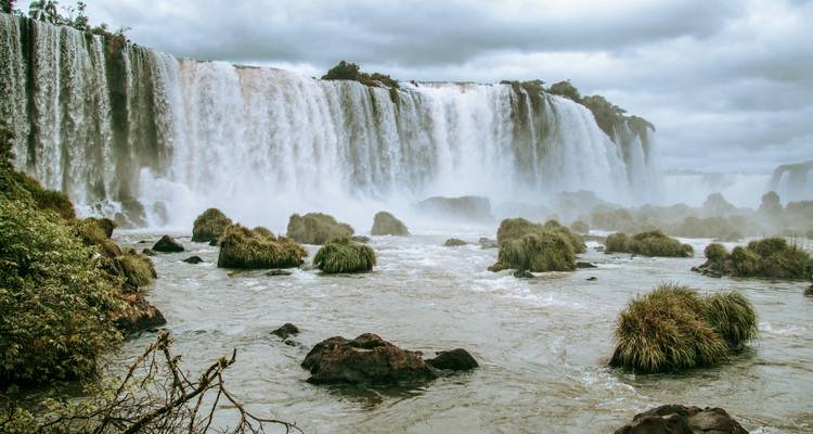 Iguazu Falls with flowing water and greenery, cloudy sky above.