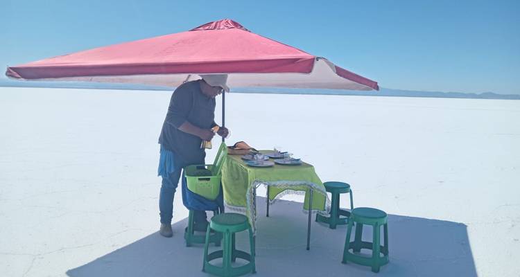 Person setting up a table under an umbrella on the Uyuni Salt Flat.