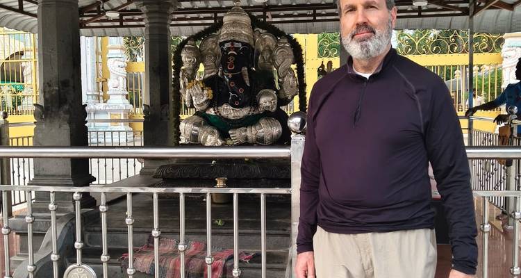 A visitor stands beside a black stone Ganesh idol enclosed by an ornate railing in a South Indian temple courtyard.