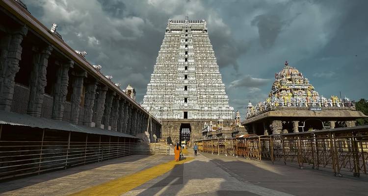 Long corridor view of a towering gopuram and inner temple complex under dramatic skies.