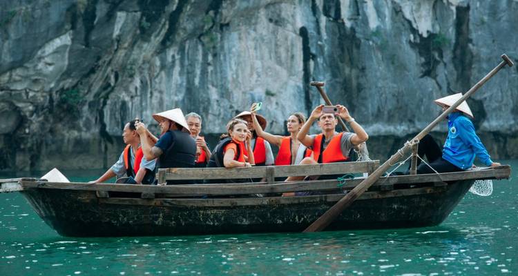 Gruppe von Menschen, die auf einem Boot Fotos machen, mit felsigen Klippen im Hintergrund.