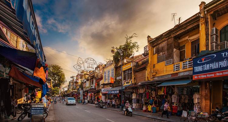 Charmante Straße mit belebten Geschäften und einer Mischung aus alter und moderner Architektur unter einem dynamischen Himmel.