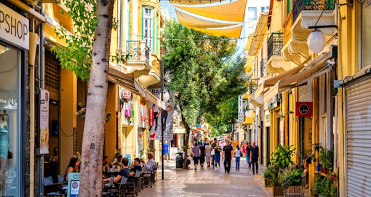 Busy street with cafes and shops, lively atmosphere with people walking.