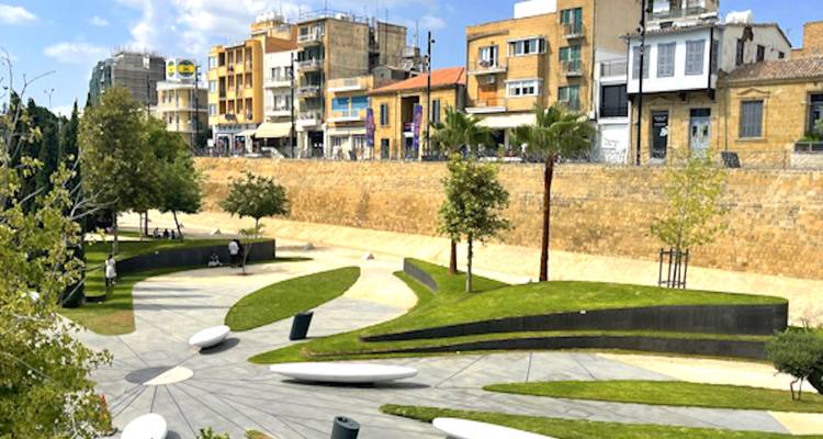 Modern park with grass and benches, lined with city buildings.