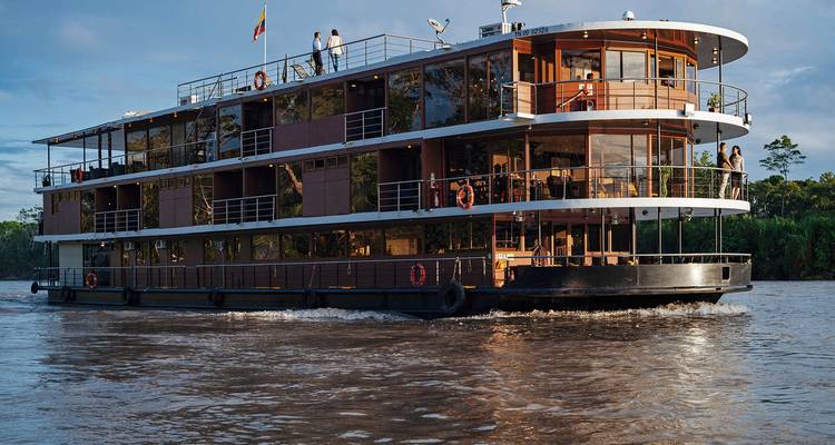 Vue de côté d'un bateau de croisière fluviale naviguant avec des passagers sur le pont.