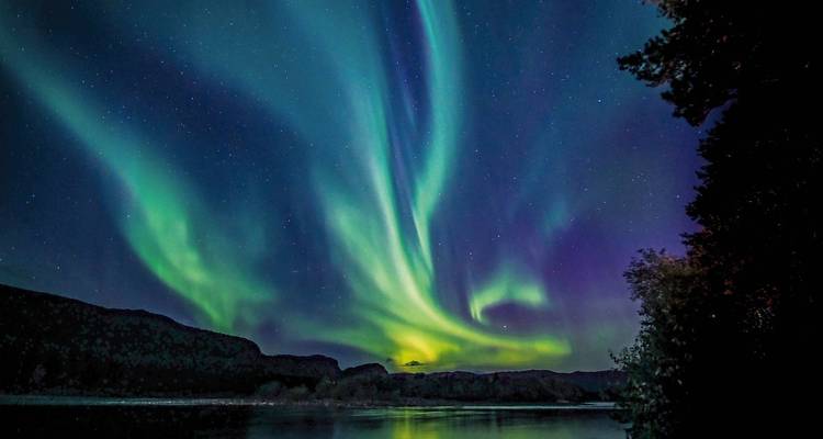 Noorderlicht boven een kalm meer in een bergachtig gebied.