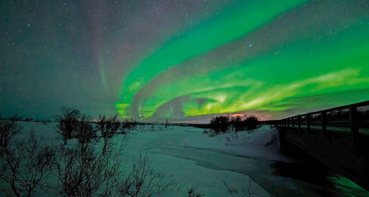Een panoramisch nachtlandschap met het noorderlicht boven een besneeuwde veld en verre heuvels.