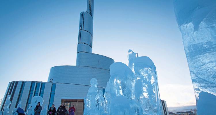 Moderne ijssculptuur buiten een hedendaags gebouw met mensen die het gebied verkennen.