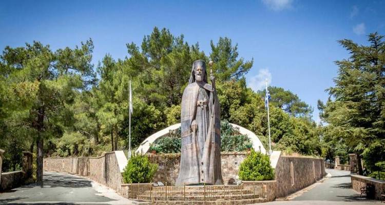 Large bronze statue of Archbishop Makarios standing amidst pine trees.