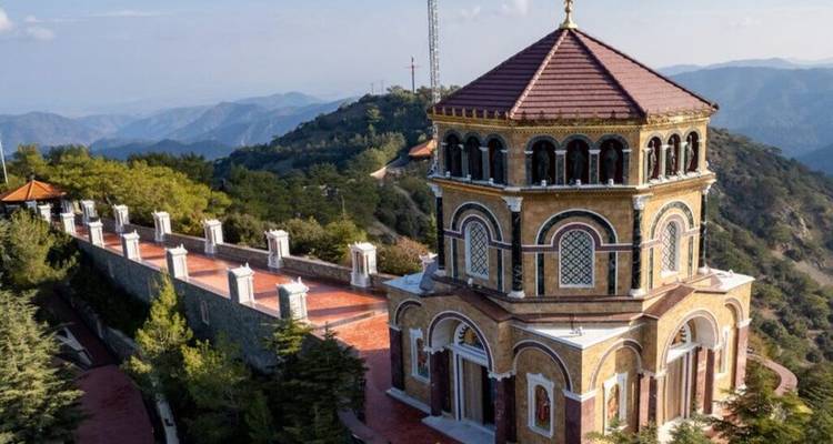 Octagonal mountaintop chapel with tiled roof overlooking rolling forested mountains.