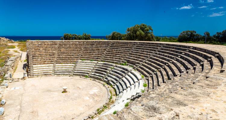 Circular ancient stone amphitheatre with tiered seating under a clear blue sky.