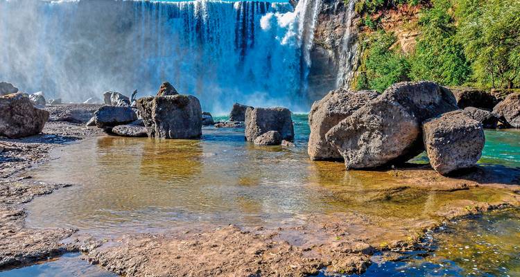 Atemberaubender Wasserfall mit Felsen im Vordergrund und üppigem Grün.