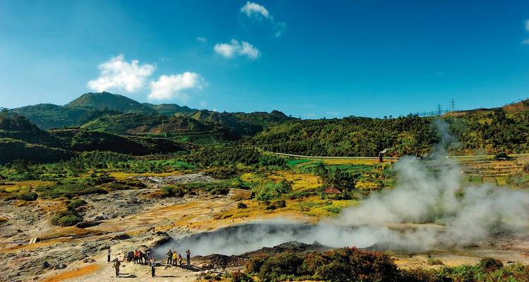 Geothermal area with steam rising from the ground in a rural setting.