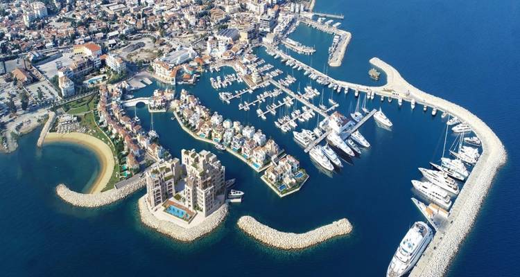 Aerial view of Limassol Marina with luxury yachts, curving breakwaters, and seafront cityscape.