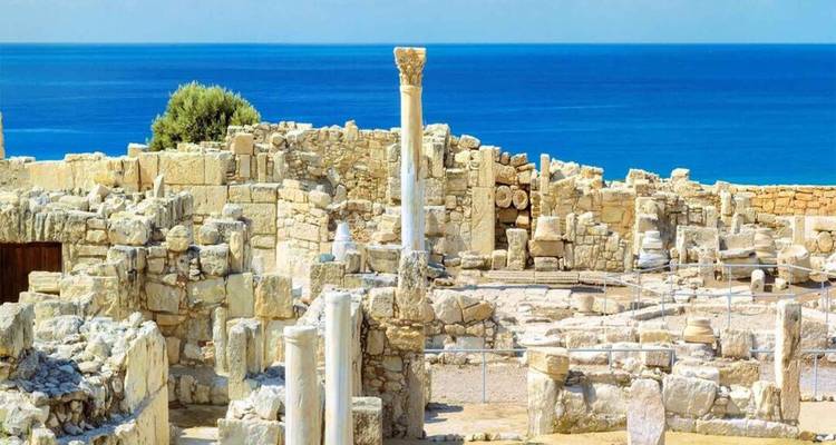 Sun-washed limestone ruins with a single standing column set against a vivid blue sea backdrop.