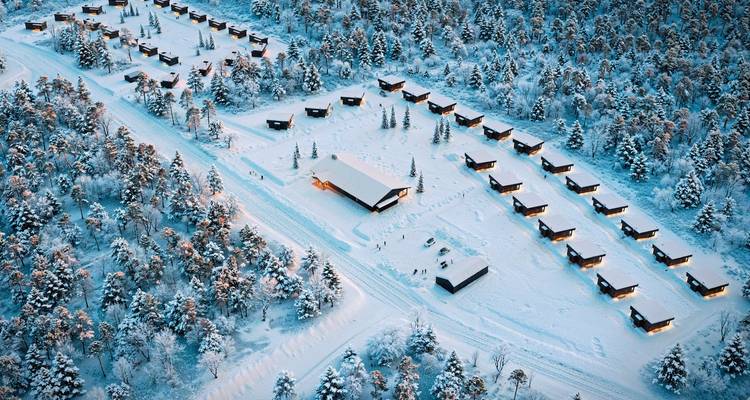Luftaufnahme einer schneebedeckten Landschaft mit Hütten zwischen Bäumen.