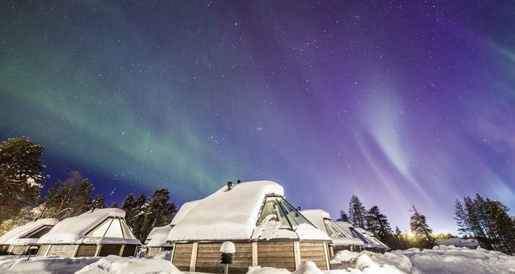 Nordlichter über schneebedeckten Hütten unter einem sternenklaren Himmel.
