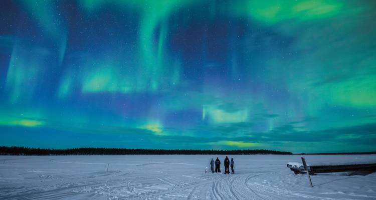 Menschen, die Nordlichter über einer verschneiten Landschaft beobachten.