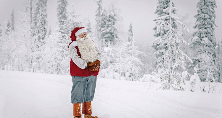 Person verkleidet als Weihnachtsmann in einer verschneiten Landschaft mit Bäumen.