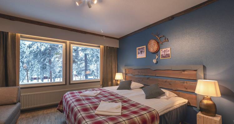 Gemütliches Hotelzimmer mit karierter Bettwäsche und verschneiter Aussicht draußen.