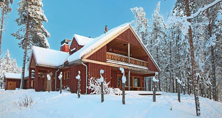 Una cabaña roja con techo cubierto de nieve rodeada de árboles nevados.